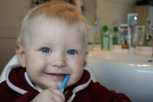Smiling toddler using a blue toothbrush